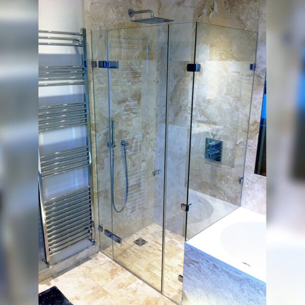 Frameless inline hinged shower door with dwarf side panel over a bath by Room H2o